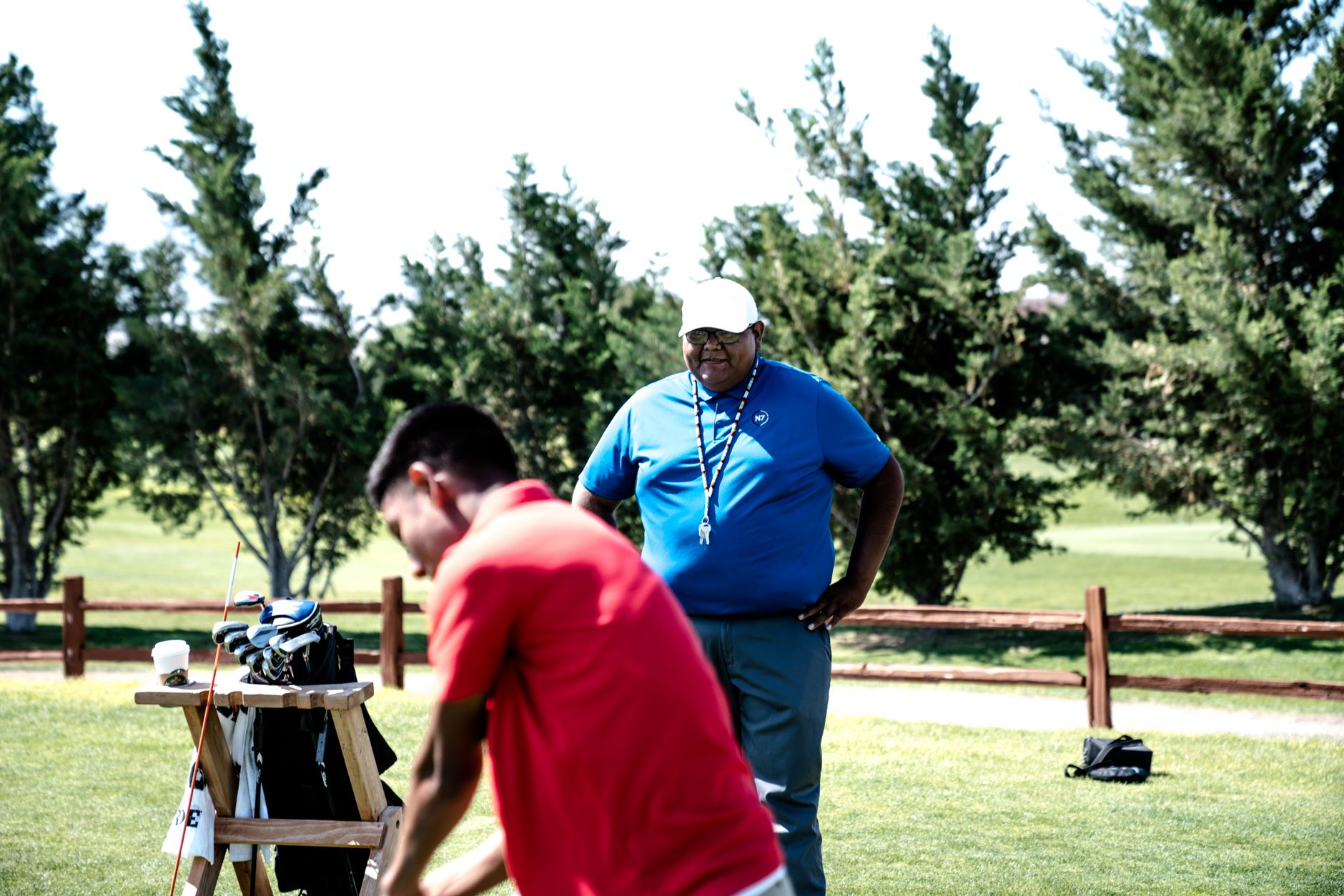 Deux personnes sur un terrain de golf, l’une observant l’autre à côté d’un sac de clubs de golf.