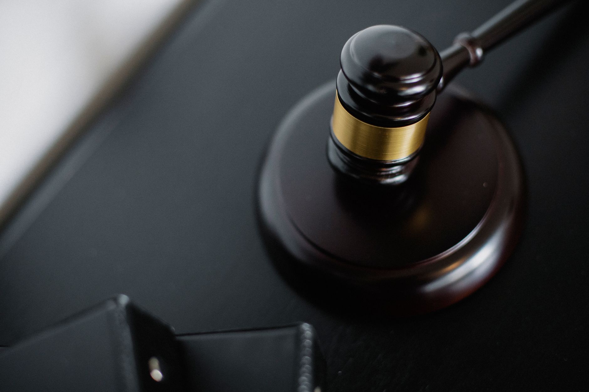 Maillet de juge en bois sombre à bague dorée, posé sur son socle rond sur une surface noire.